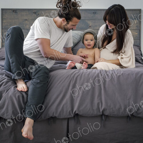 A young couple and their young son sitting together on their bed.
