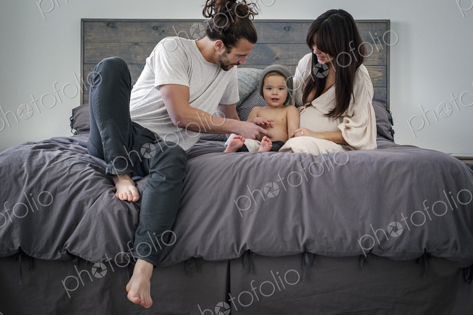 A young couple and their young son sitting together on their bed.