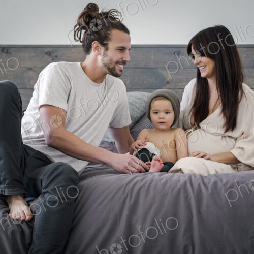 A young couple and their young son sitting together on their bed.