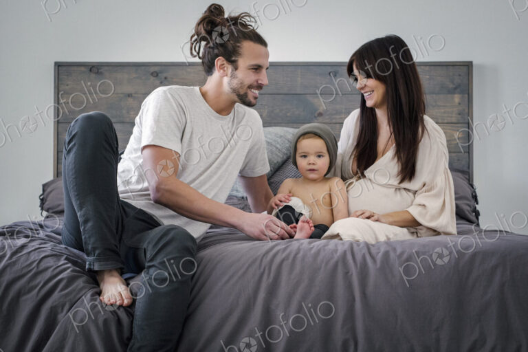 A young couple and their young son sitting together on their bed.