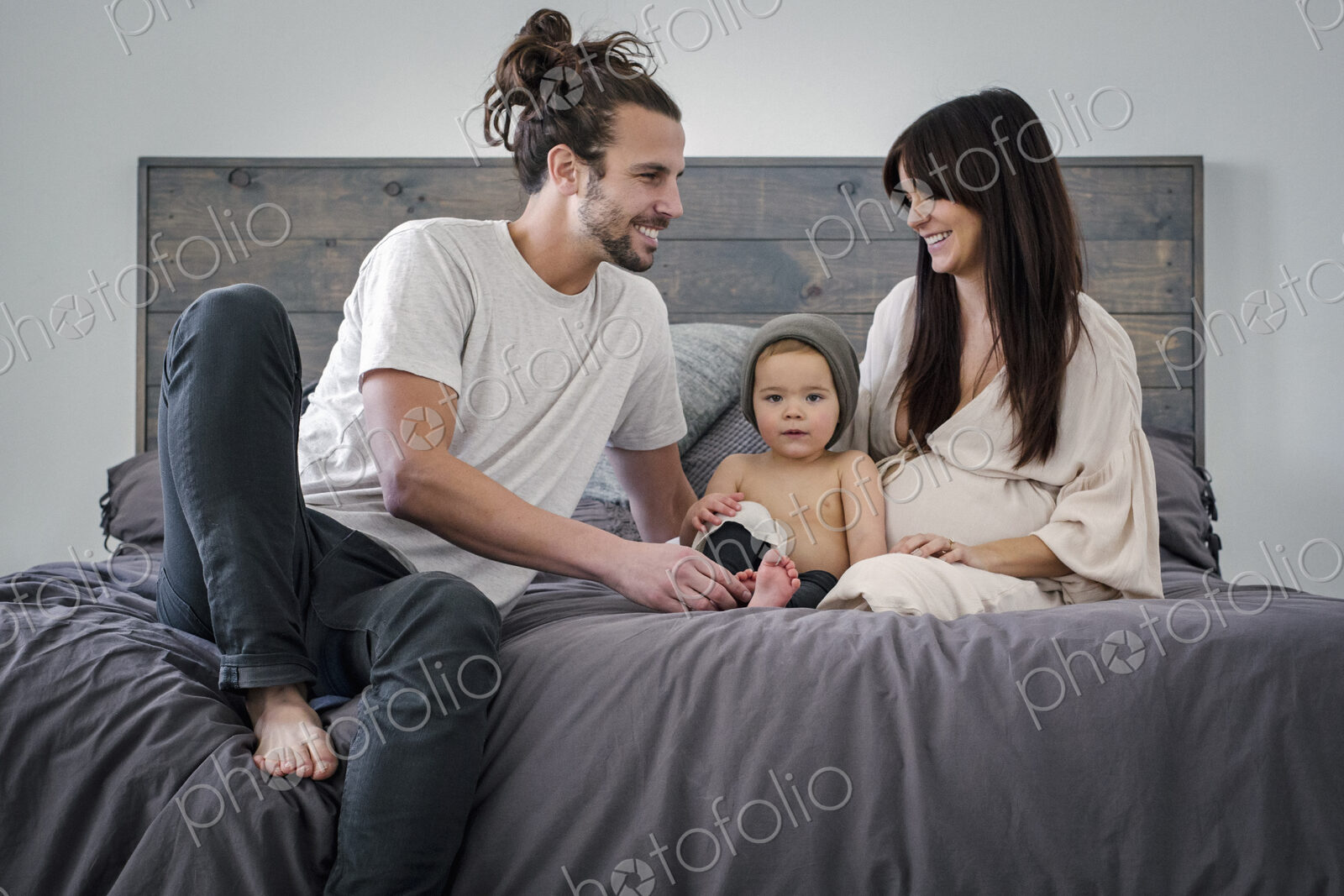 A young couple and their young son sitting together on their bed.