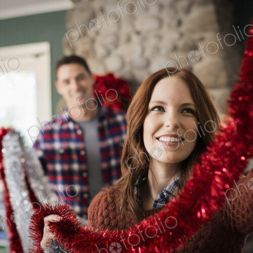 A young couple hanging tinsel up, decorating a house at Christmas.