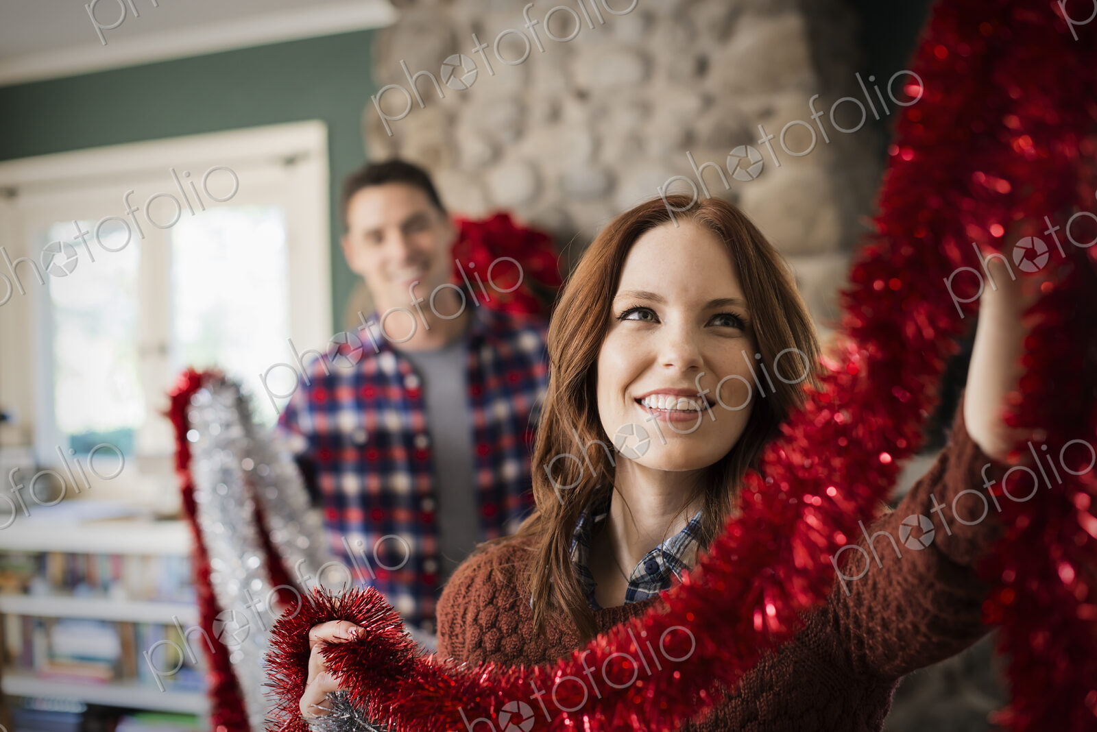A young couple hanging tinsel up, decorating a house at Christmas.