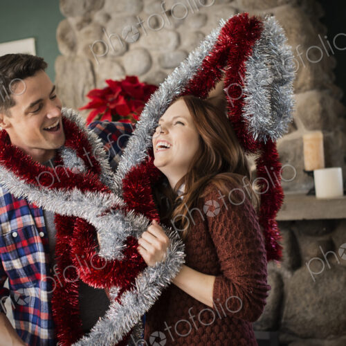 A young couple hanging tinsel up, decorating a house at Christmas.