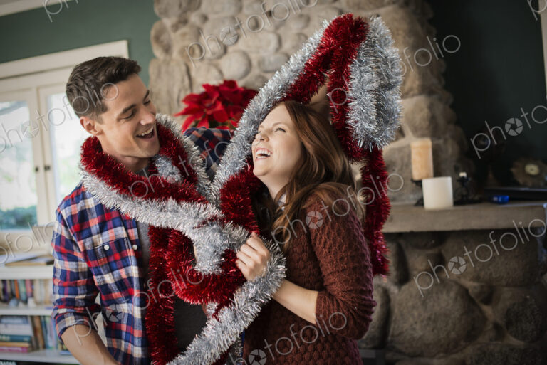 A young couple hanging tinsel up, decorating a house at Christmas.