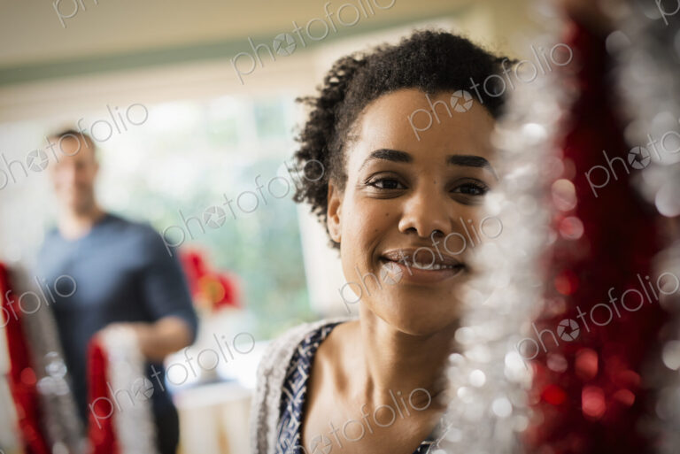 A young couple hanging tinsel up, decorating a house at Christmas.
