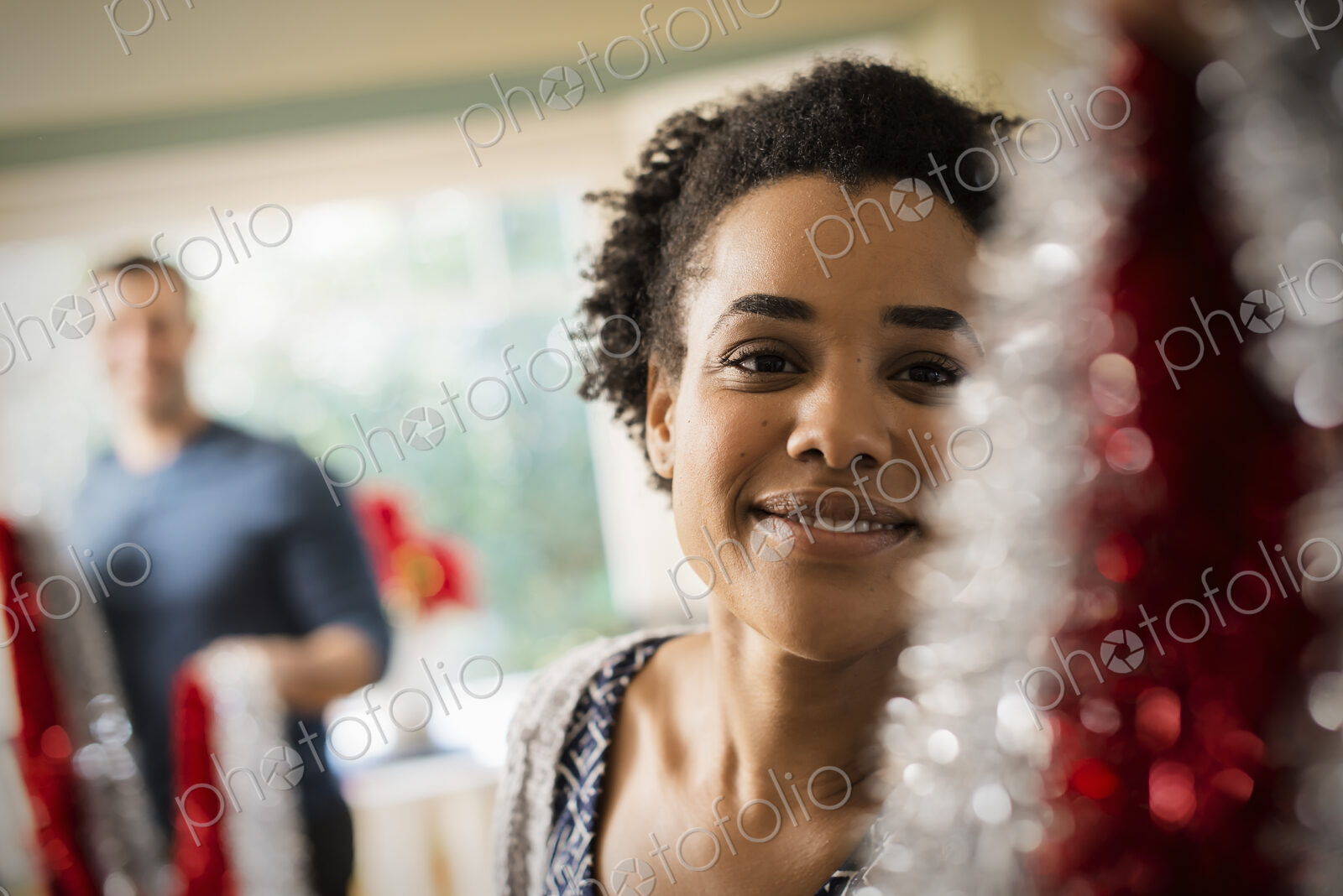 A young couple hanging tinsel up, decorating a house at Christmas.