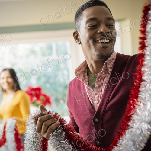 A young couple hanging tinsel up, decorating a house at Christmas.