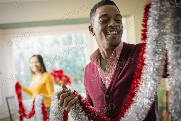A young couple hanging tinsel up, decorating a house at Christmas.