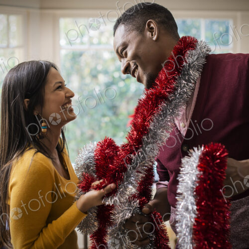 A young couple hanging tinsel up, decorating a house at Christmas.