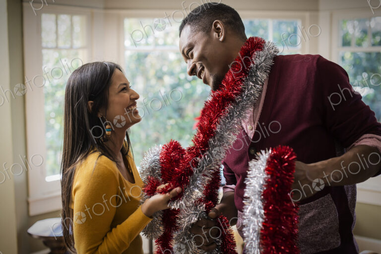 A young couple hanging tinsel up, decorating a house at Christmas.