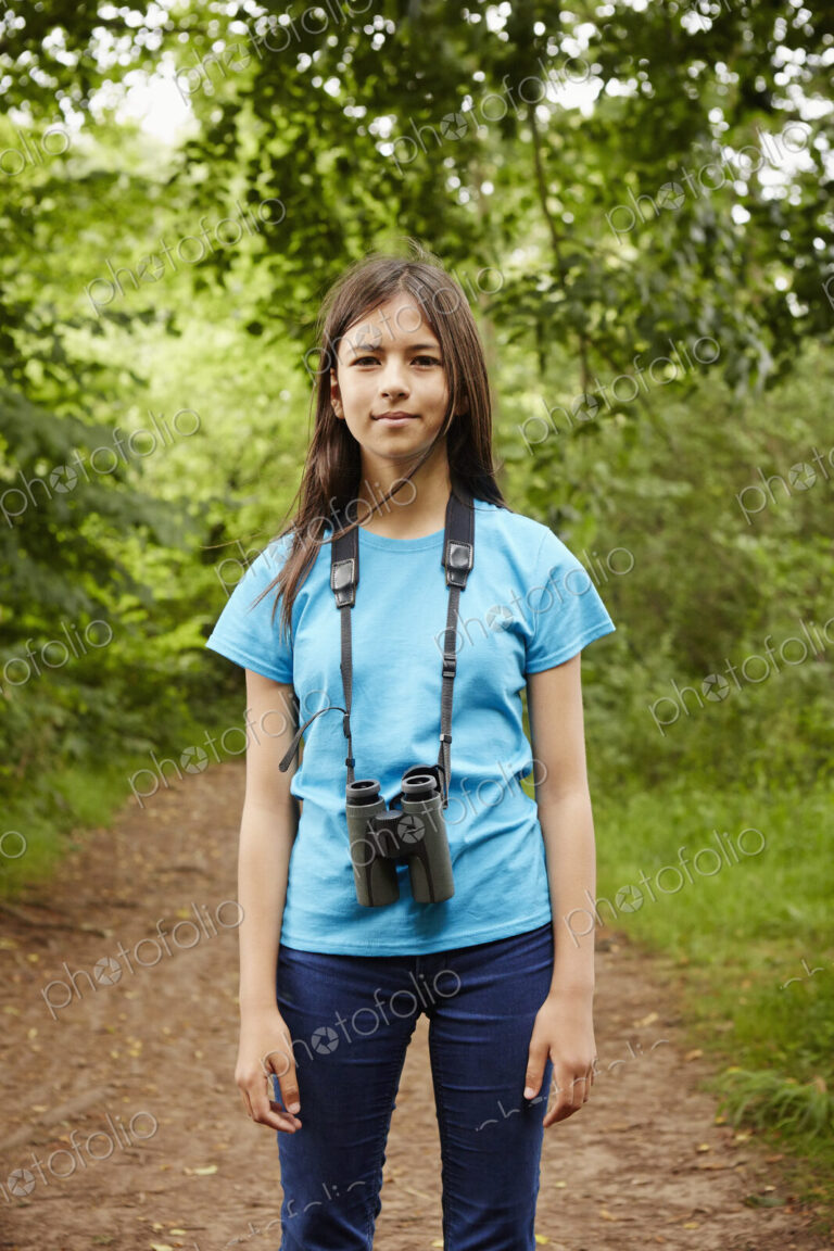 A young girl, a birdwatcher in a wood with binoculars around her neck.