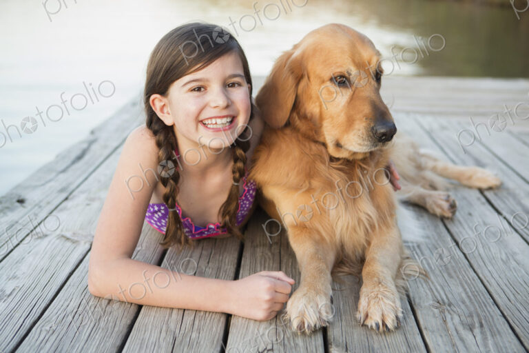 A young girl and a golden retriever dog lying on a jetty.