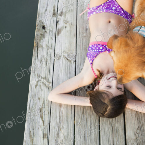 A young girl and a golden retriever dog on a jetty.