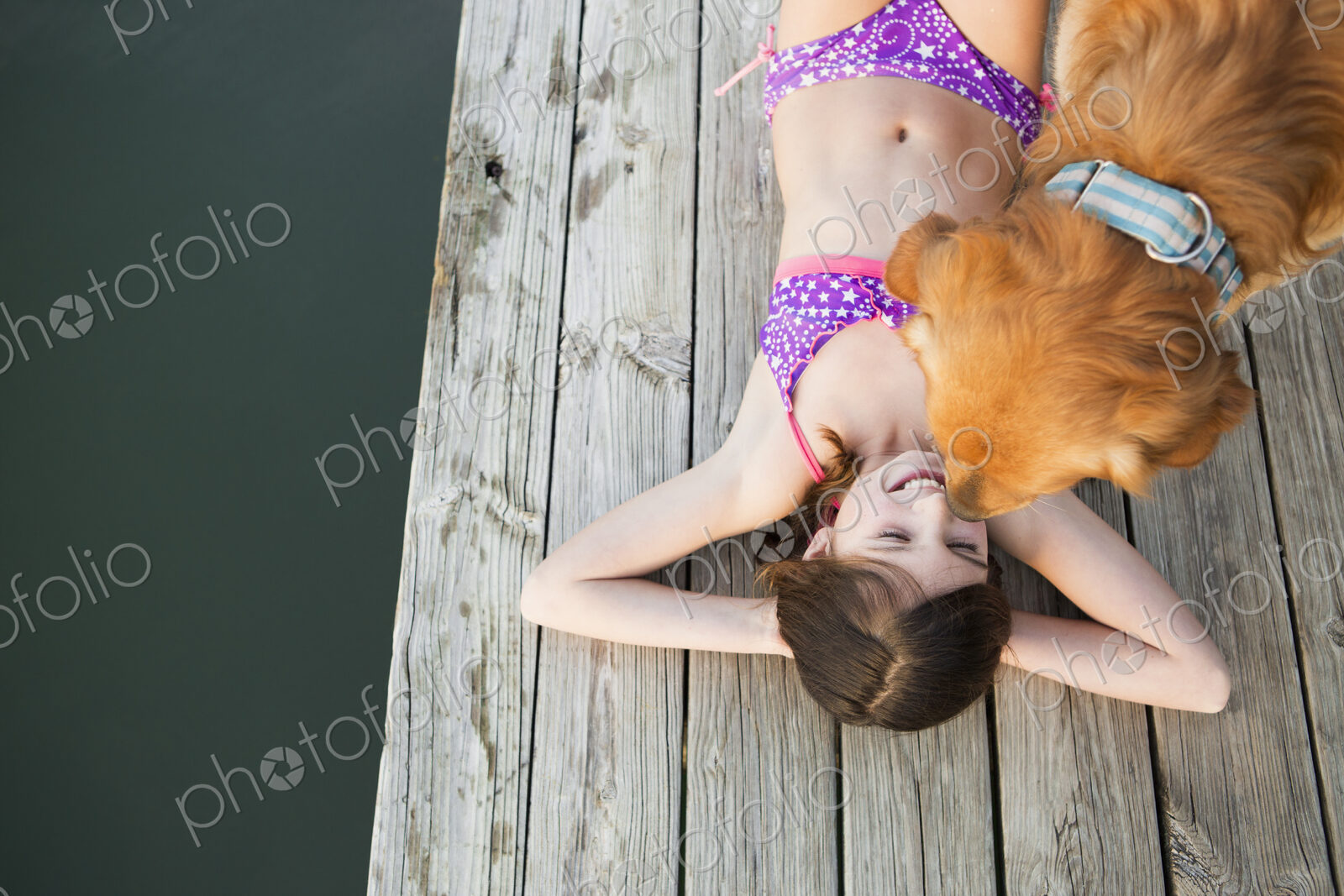 A young girl and a golden retriever dog on a jetty.