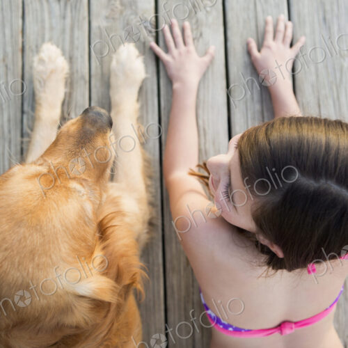 A young girl and a golden retriever dog side by side on a jetty.