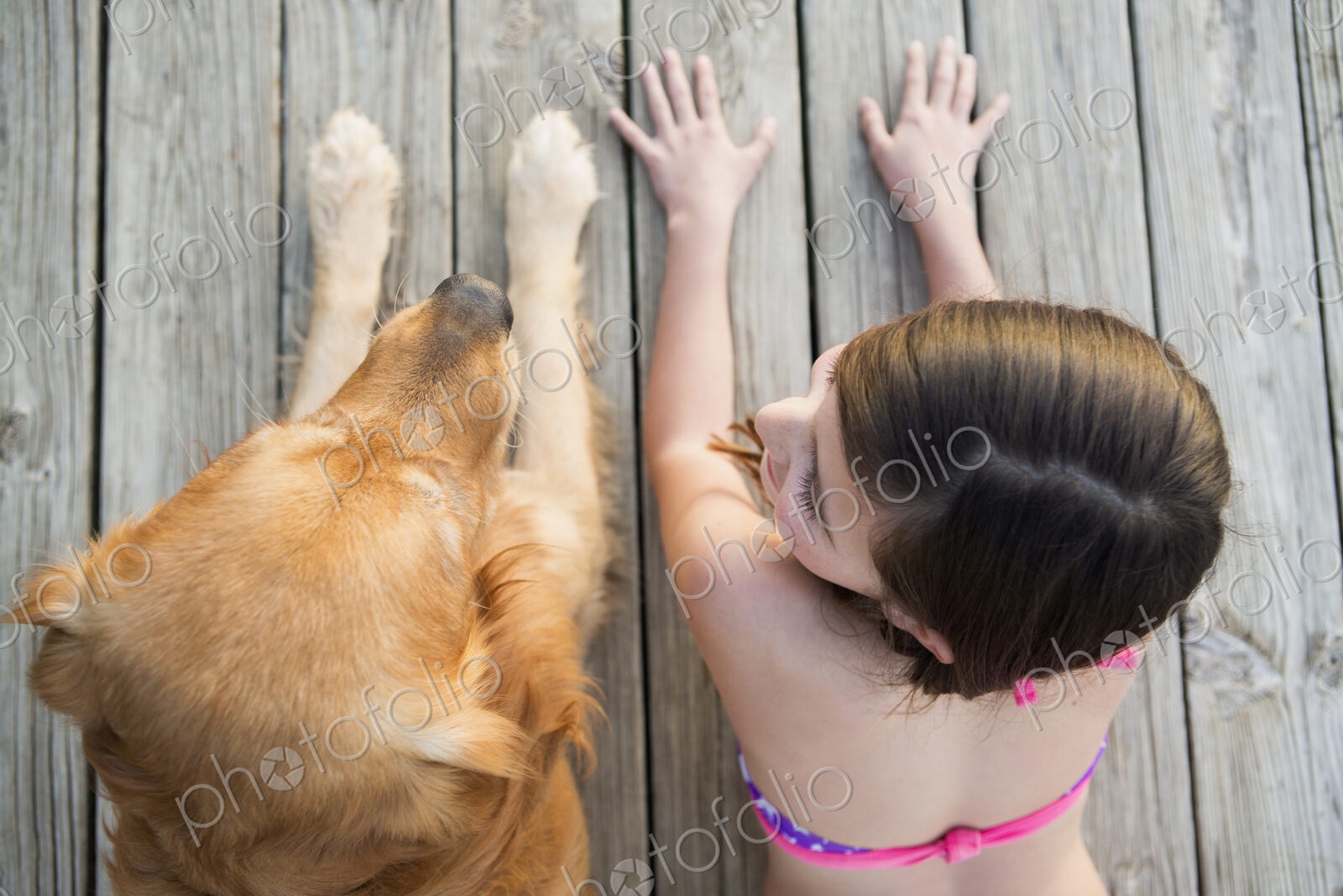 A young girl and a golden retriever dog side by side on a jetty.