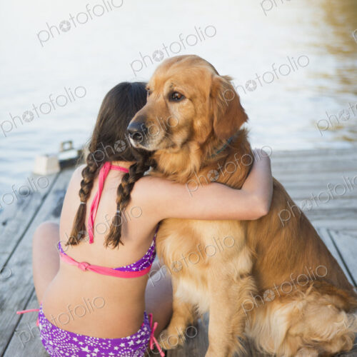 A young girl and a golden retriever dog sitting on a jetty.