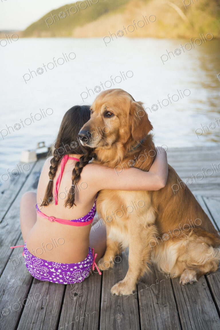 A young girl and a golden retriever dog sitting on a jetty.