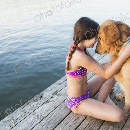 A young girl and a golden retriever dog sitting on a jetty.