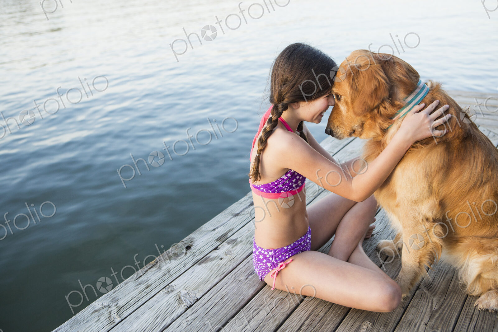 A young girl and a golden retriever dog sitting on a jetty.