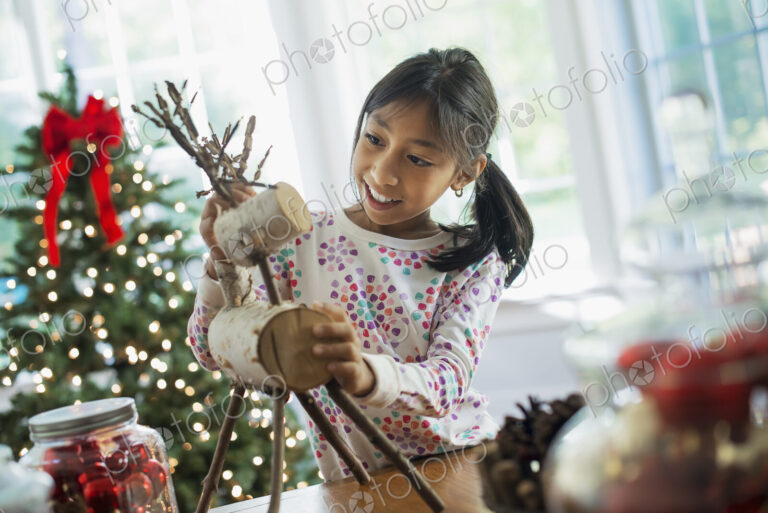 A young girl assembling a twig figure of a reindeer, making Christmas decorations.