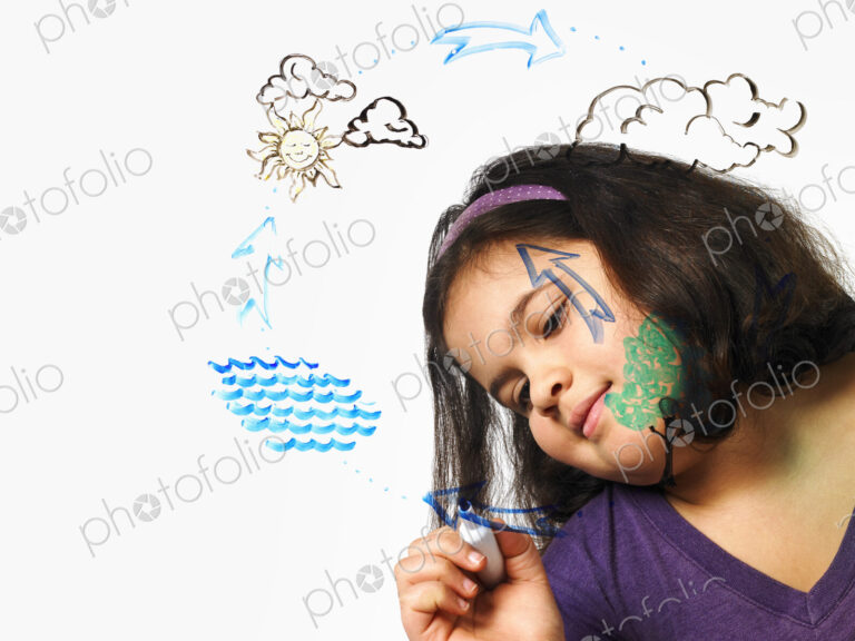 A young girl drawing the water evaporation cycle on a clear see through surface with a…