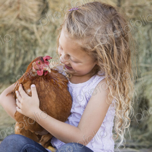 A young girl holding a chicken in a henhouse.