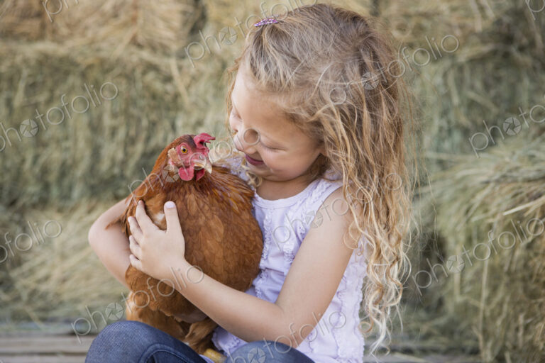 A young girl holding a chicken in a henhouse.