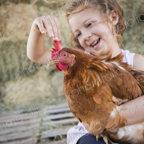 A young girl holding a chicken in a henhouse.