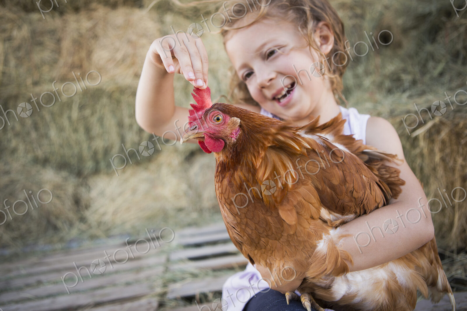 A young girl holding a chicken in a henhouse.