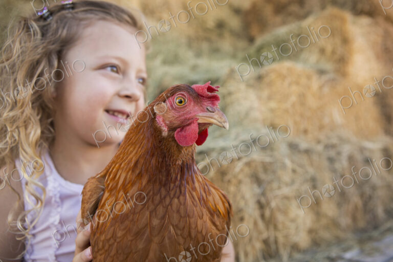 A young girl holding a chicken in a henhouse.