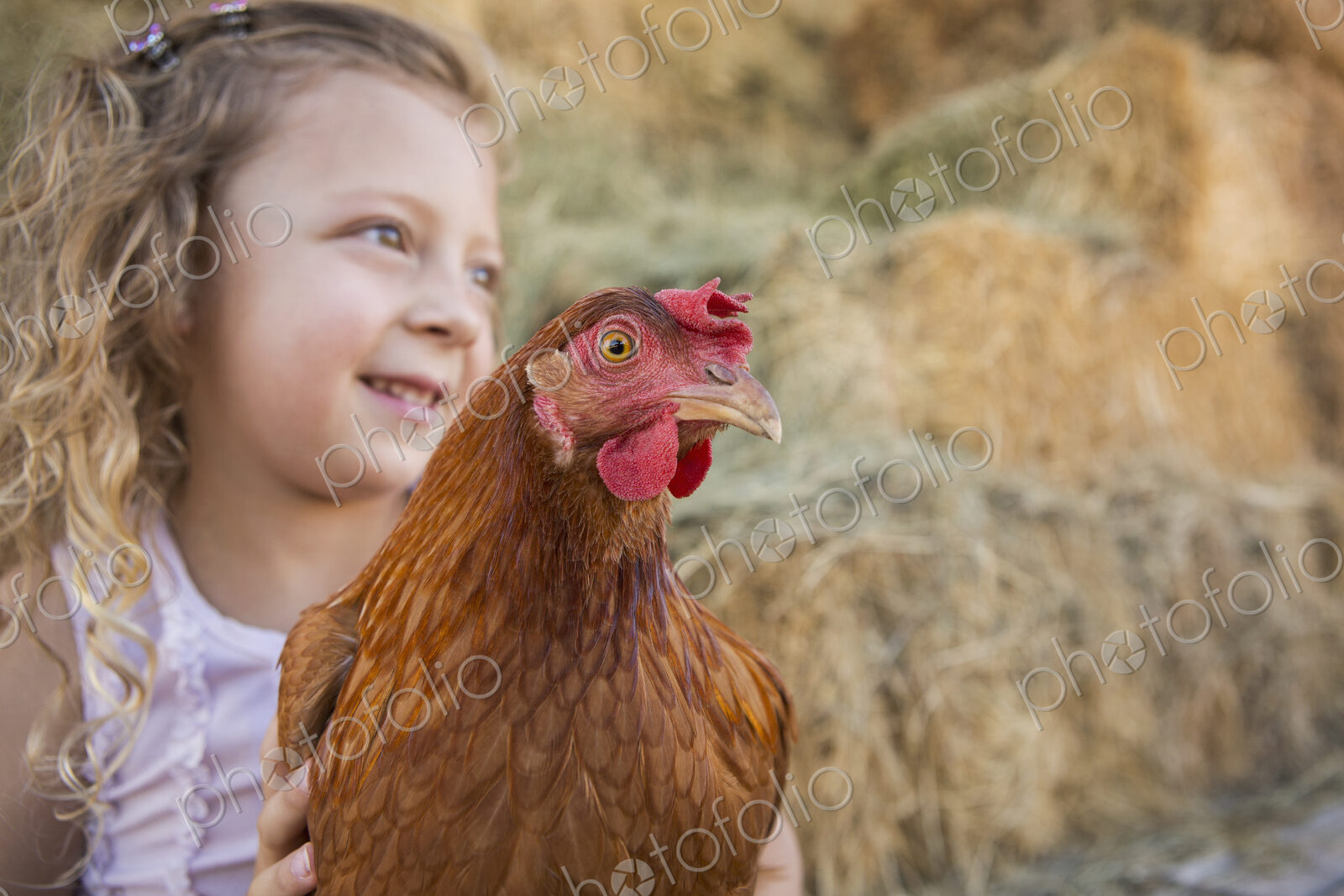 A young girl holding a chicken in a henhouse.