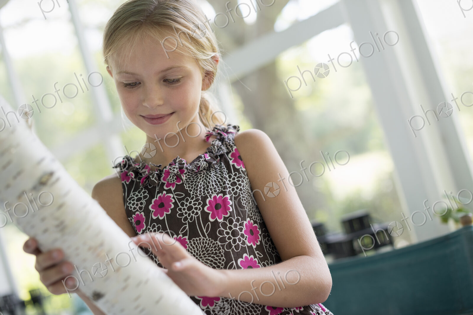 A young girl holding a piece of tree trunk with very white bark.