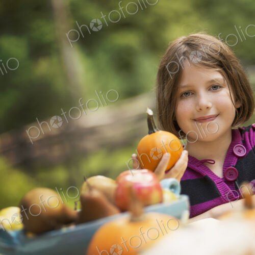 A young girl holding a pumpkin in her hand at a table outside. Harvest time. A young girl holding a pumpkin in her hand at a table outside. Harvest time.