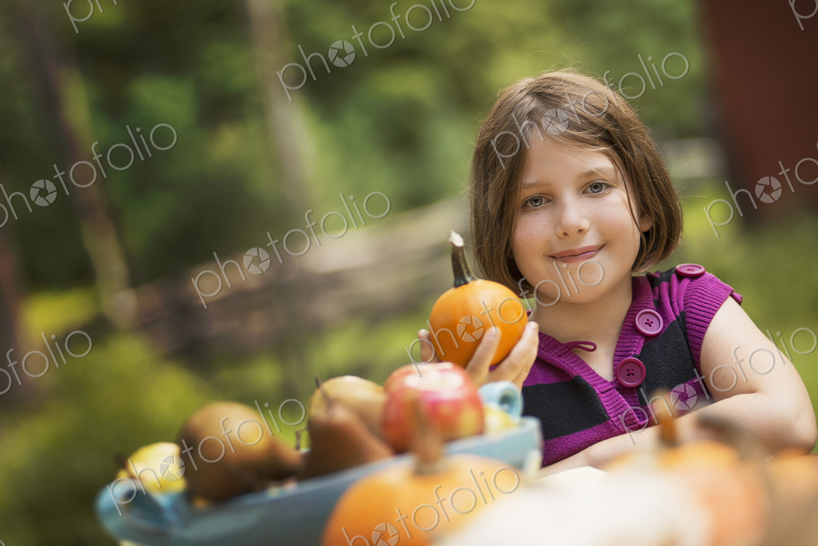 A young girl holding a pumpkin in her hand at a table outside. Harvest time.
