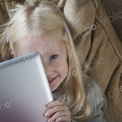 A young girl holding a silver laptop in front of her face.