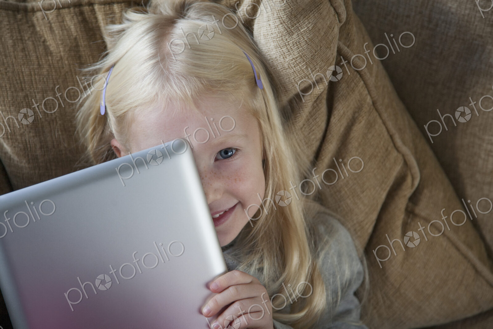 A young girl holding a silver laptop in front of her face.