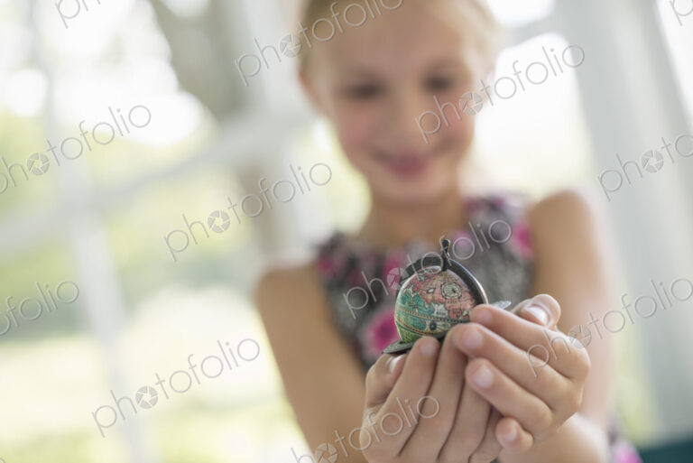 A young girl holding out a small globe in the palms of her cupped hands.