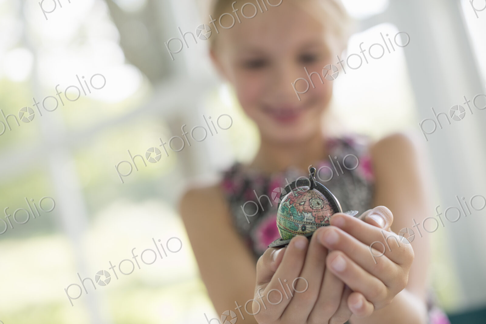 A young girl holding out a small globe in the palms of her cupped hands.