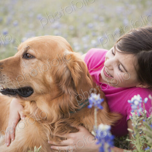 A young girl hugging a golden retriever pet.