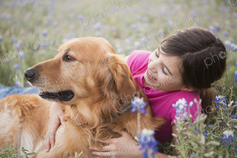 A young girl hugging a golden retriever pet.