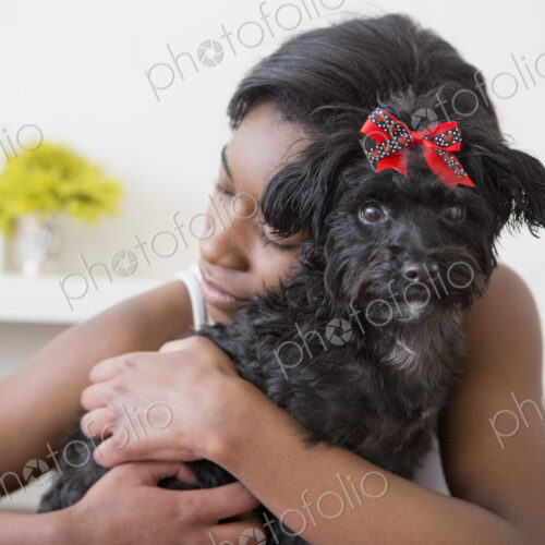 A young girl hugging her small black pet dog.
