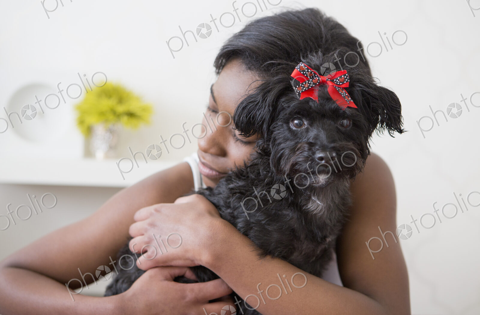 A young girl hugging her small black pet dog.