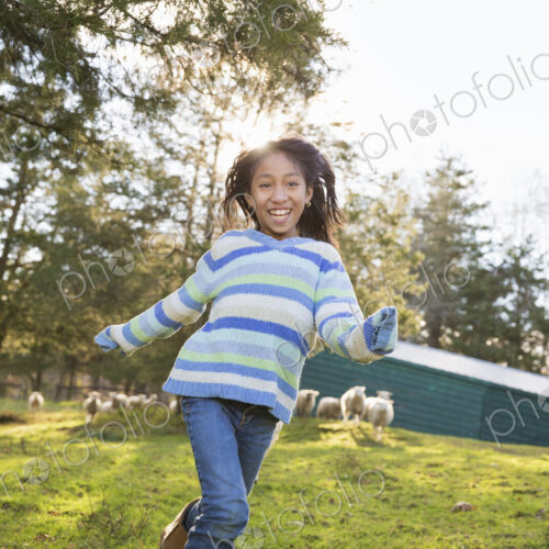 A young girl in a blue stripey top running in a field of sheep at an animal sanctuary. A young girl in a blue stripey top running in a field of sheep at an animal sanctuary.