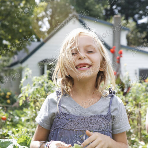 A young girl in a blue teeshirt and pinafore dress laughing, and holding green beans… A young girl in a blue teeshirt and pinafore dress laughing, and holding green beans…