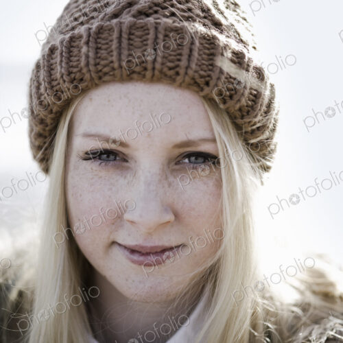 A young girl in a bobble hat on the beach.
