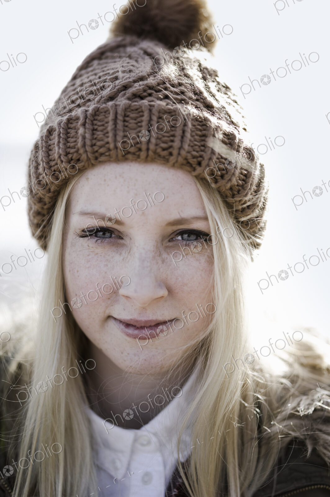 A young girl in a bobble hat on the beach.