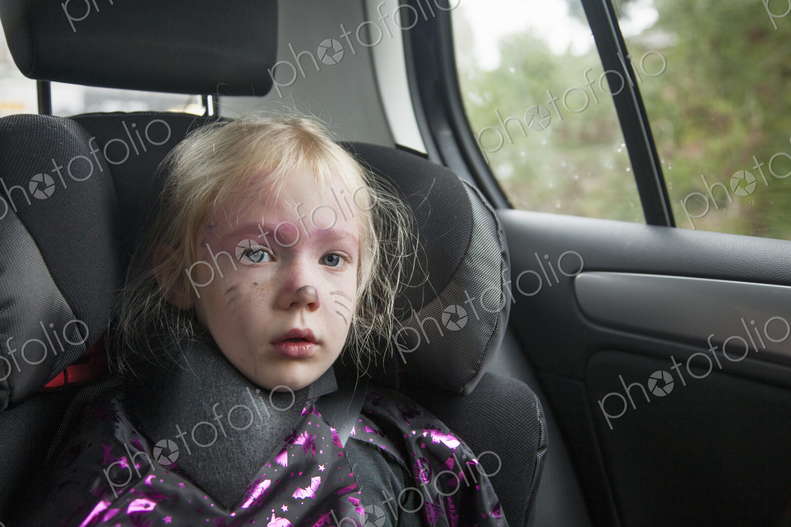A young girl in a car seat in Halloween costume.