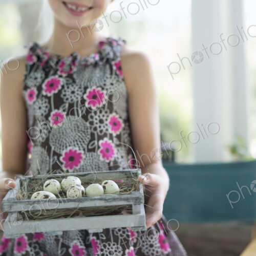 A young girl in a floral dress, examining a clutch of speckled bird eggs in a box. A young girl in a floral dress, examining a clutch of speckled bird eggs in a box.